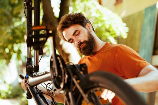 Focused young man thoroughly examining his bike tire for rubber damages during his yearly maintenance routine. Committed male cyclist ensuring modern bicycle is in top condition for leisure activity.