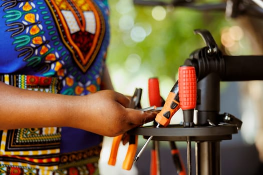 Close up of person choosing expert work tools for yearly outdoor bicycle maintenance. Detailed shot of female african american arm arranging an assortment of professional equipments.