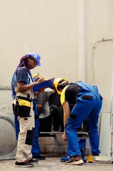 Diverse crew of trained engineers fixing air conditioner system electrical issues caused by faulty wiring or defective capacitor requiring professional intervention to diagnose and repair