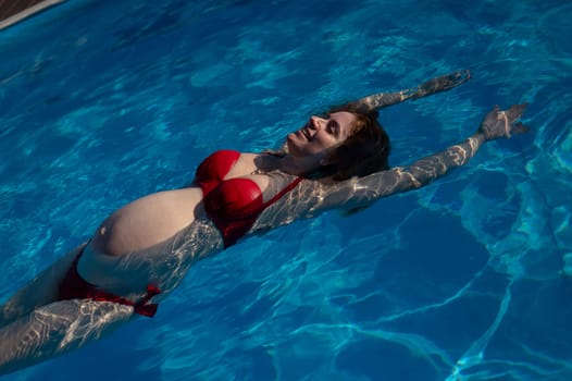 Top view of pregnant woman floating in pool in red bikini