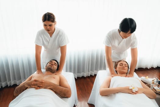 Caucasian couple customer enjoying relaxing anti-stress spa massage and pampering with beauty skin recreation leisure in day light ambient salon spa at luxury resort or hotel. Quiescent