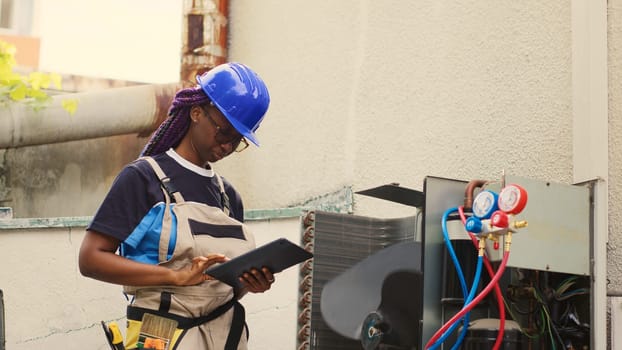 Seasoned mechanic servicing external condenser internal parts, checking refrigerant level and calibrating thermostats. Capable electrician imputing maintenance results data on laptop