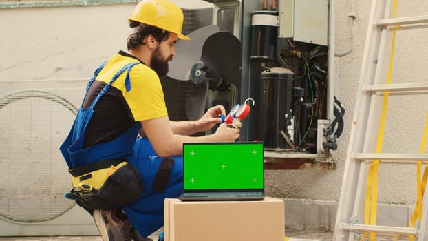 Seasoned mechanic employed by customer to find cause of faulty outdoor hvac system using measurement device, with nitrogen pressure loss over time displayed on chroma key laptop screen