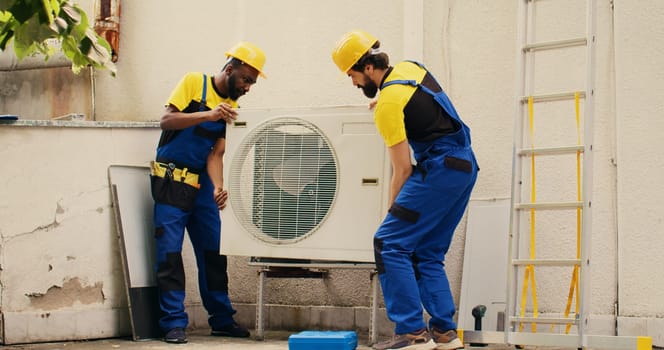 Certified technicians coworkers opening up rusty malfunctioning air conditioner to replace it with new performant outside condenser after draining refrigerant and replacing ductwork