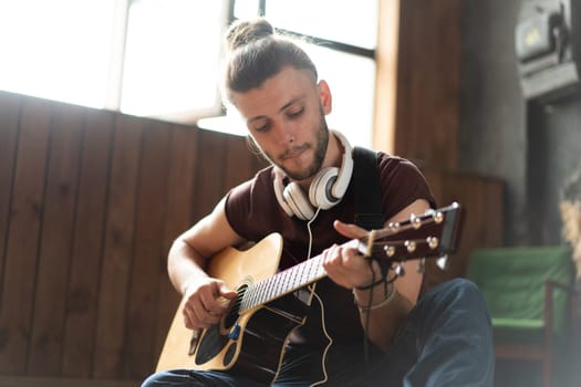 Handsome young man playing acoustic guitar sitting floor living loft room Caucasian male hipster headphones guitar player practicing singing enjoy music relaxing Creative modern young guy Medium shoot