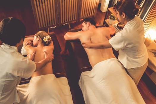 Caucasian couple customer enjoying relaxing anti-stress spa massage and pampering with beauty skin recreation leisure in warm candle lighting ambient salon spa at luxury resort or hotel. Quiescent