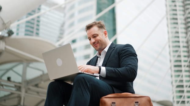 Low angle view of professional business man working on laptop at stairs. Caucasian project manager using computer to plan marketing strategy and communicate with financial team at urban city. Urbane.