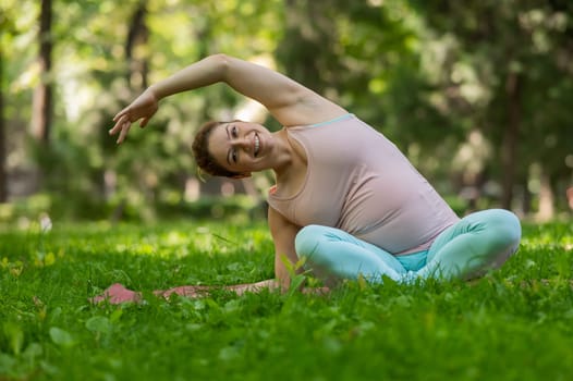 Pregnant caucasian woman doing yoga in the park. Lateral tilt