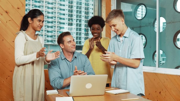 Highschool boy presenting project while teacher looking at laptop. Group of diverse student standing and explain plan while smart instructor listening and giving advise.Teamwork concept. Edification.