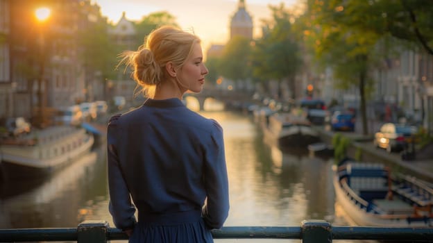 A woman in a blue dress stands on a bridge overlooking a canal. The scene is serene and peaceful, with the sun setting in the background. The woman is enjoying the view