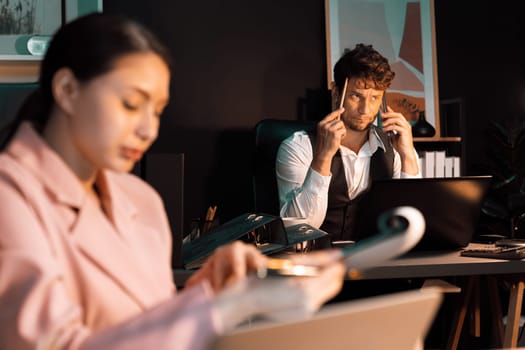 Focusing businessman calling with customer for creative business project planning at back view at night light modern office with fronted view blurry secretary checking paperwork report. Postulate.