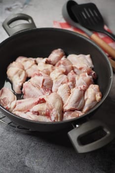 Chicken wings cooking in a pan with wooden spoons nearby.