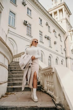 A woman wearing a white shirt and a tan coat is walking up a set of stairs. She is carrying a handbag and she is in a hurry. Concept of urgency and movement