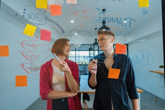 Couple of young creative start up business people brainstorming idea and solving problems by using sticky note and mind map at glass board, meeting room. discussing, working together. Immaculate.