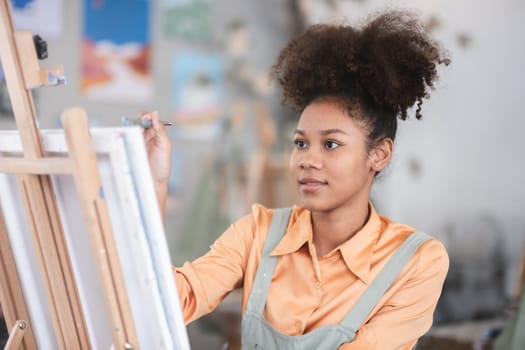 A young black artist paints acrylic paints on canvas with determination in her painting studio.