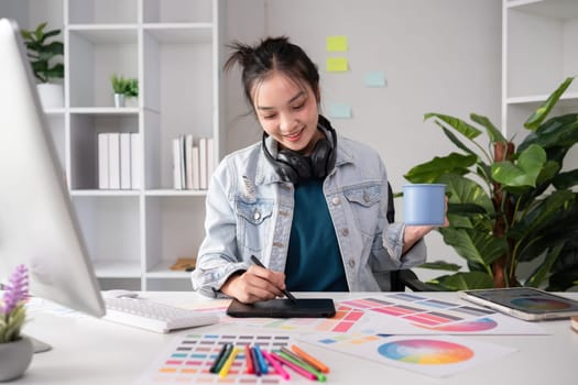 Female designer wearing headphones listening to music while doing graphic design work Choose colors for working with the computer at the table..