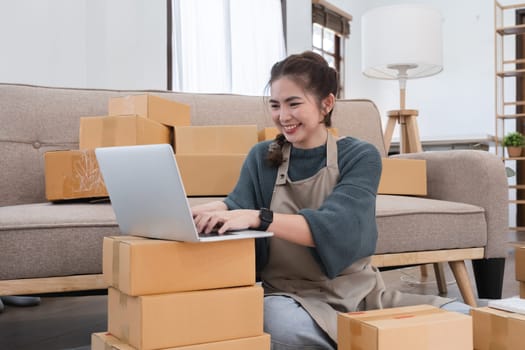 Young woman, small business owner selling products online, accepting online product orders via laptop, sits in a room with boxes of products..