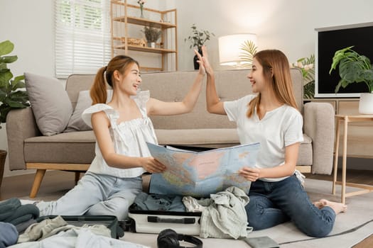 Two young female friends have fun packing supplies and clothes and discussing plans for a vacation together..