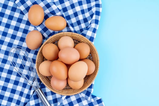 Fresh raw eggs in the basket on blue tablecloth and background.