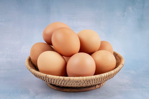 Freshness chicken eggs in wooden weave basket on blue background.