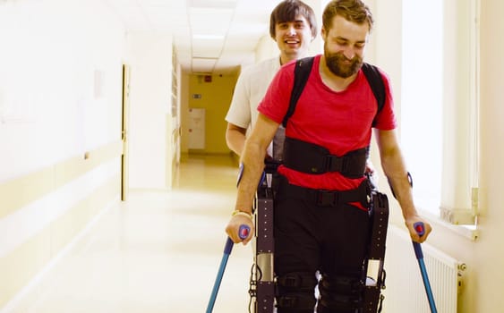 Young disable man in the robotic exoskeleton sitting in wheelchair in the rehabilitation clinic