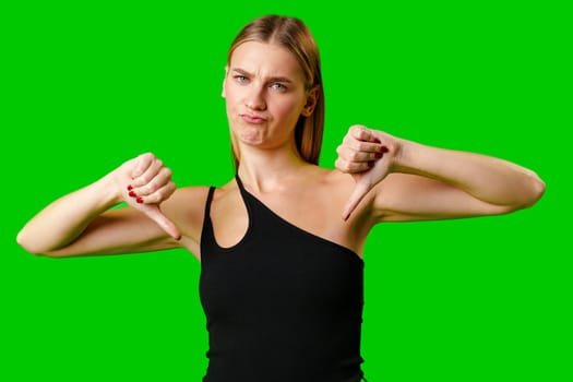 Young Woman Expressing Disapproval With a Thumbs Down Gesture Against a Green Background in studio