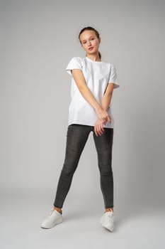 Beautiful young girl posing in white T-shirt and jeans on gray background in studio