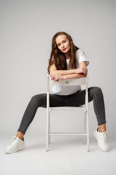 Curly girl model posing on a chair against gray background in studio