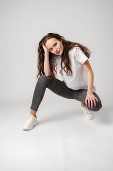 Beautiful young girl posing in white T-shirt and jeans on gray background in studio