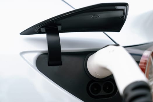 Closeup EV charger plug handle attached to electric vehicle port, recharging battery from charging station. Modern designed EV car and clean energy sustainability for better future concept. Synchronos