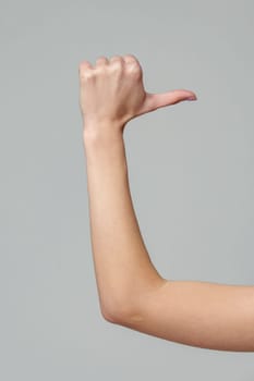 Female hand gesturing thumb up sign on gray background close up