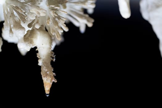 Unique view of a stalactite forming from a water droplet in a dark cave with space for text on black background.