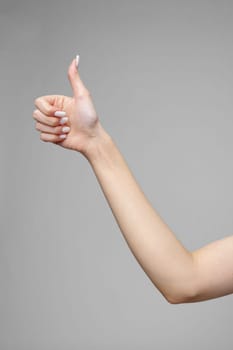 Female hand gesturing sign against gray background close up