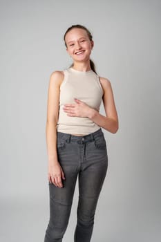 Girl in Beige Tank Top and Grey Jeans on gray background in studio