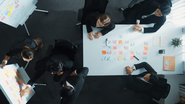 Top down aerial view of business group sharing and brainstorming idea by using sticky notes at meeting room. Investor writing marketing strategy on board while receive note from manager. Directorate.