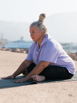 Mature woman with dreadlocks working out doing yoga exercises on sea beach - wellness well-being and active elderly age.