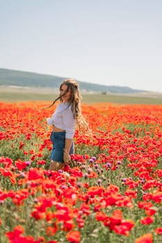 Happy woman in a poppy field in a white shirt and denim skirt with a wreath of poppies on her head posing and enjoying the poppy field