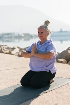 Mindful senior woman with dreadlocks meditating by the sea and beach - wellness and yoga practice concept