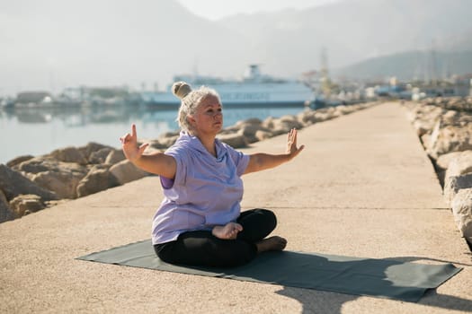 Mature old woman practicing yoga and tai chi outdoors by the sea - wellbeing and wellness concept