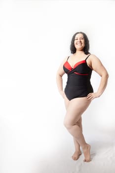 Portrait of attractive dreamy thick woman in red black swimsuit posing on white background. Body positive, photoshoot, selfie. Funny plus size model