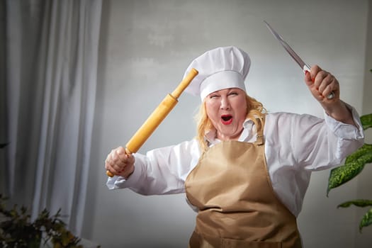 Fat evil angry funny female cook in a hat, apron and rolling pin posing and taking selfie in the kitchen. Good cooking and body positive