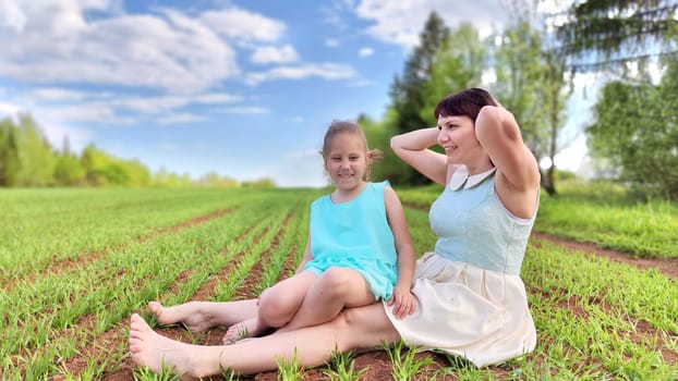 Happy mother and daughter enjoying rest, playing and fun on nature in green field. Woman and girl resting outdoors in summer or spring day
