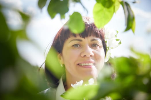 Girl walking, Relaxing near Blossoming apple Tree on Sunny Day. Portrait of Middle aged woman enjoying nature surrounded by white blossoms