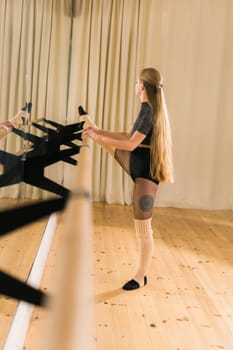 Female ballet dancer practicing at barre in dance studio - dance and ballerina