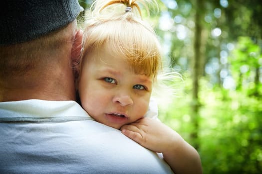 Gentle Father Holding Young Daughter Outdoors in Daylight. A tender moment as dad embraces his little girl in a sunny garden