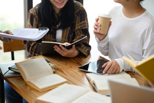 Group of college students working together for their project at table with books and laptop.