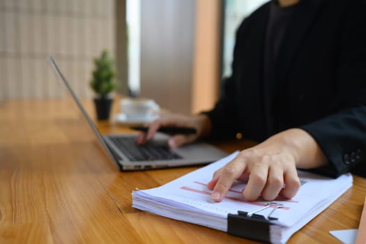 Businessman analyzing marketing data and using laptop on wooden table in office.