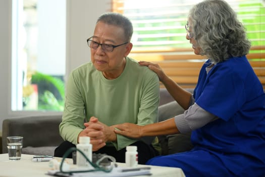 Caring doctor touching shoulder comforting upset patient during home visit. Health care concept.