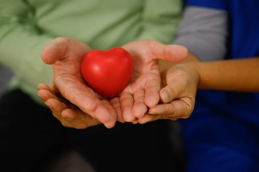 Hands of elderly couple holding red heart. Love, health care, medical and charity concept.