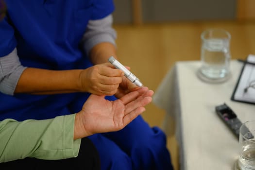 Medical worker using lancet on finger to checking blood sugar level senior patient at home.